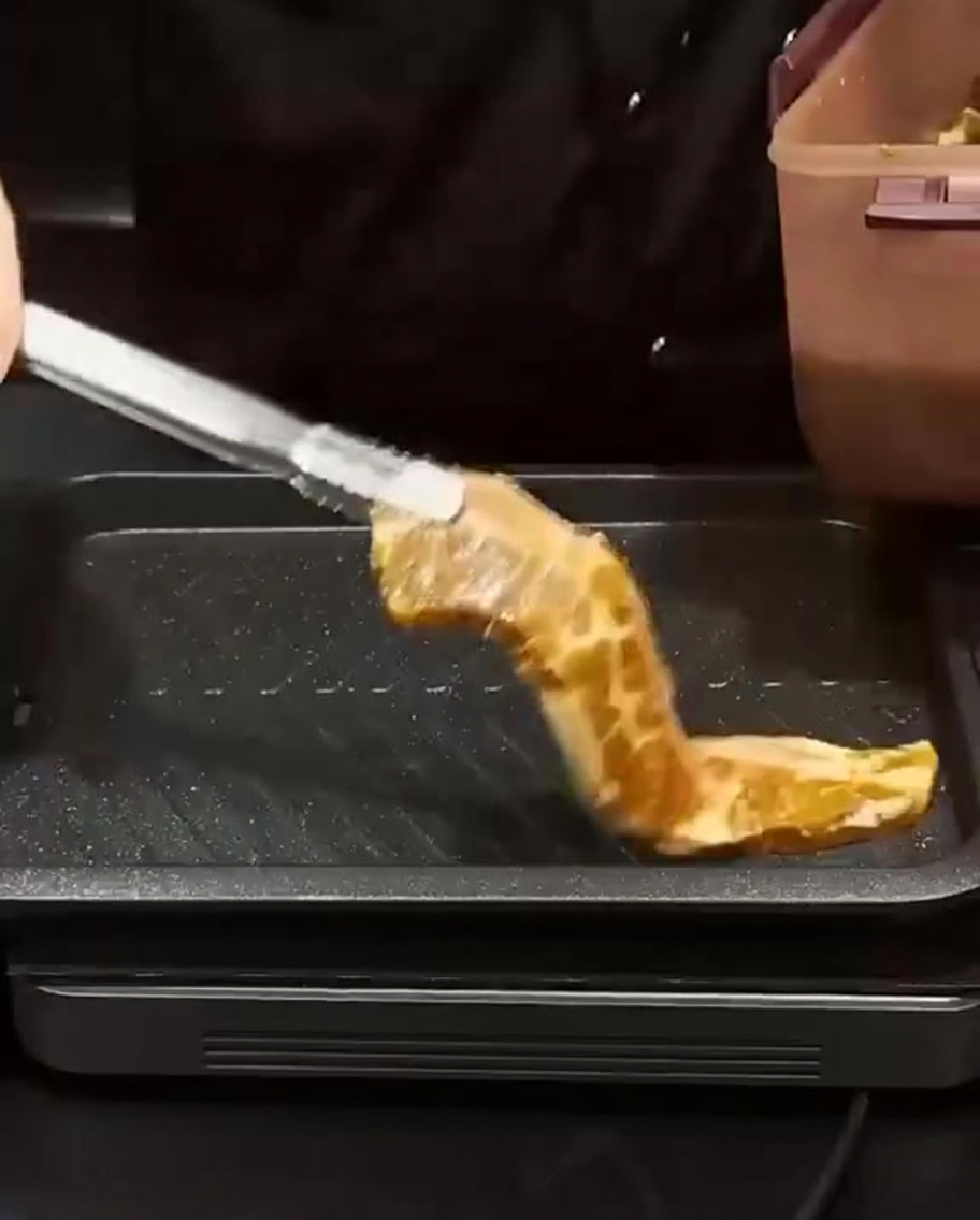 Costine marinate posizionate con una pinza su una piastra rettangolare calda per rosolare.