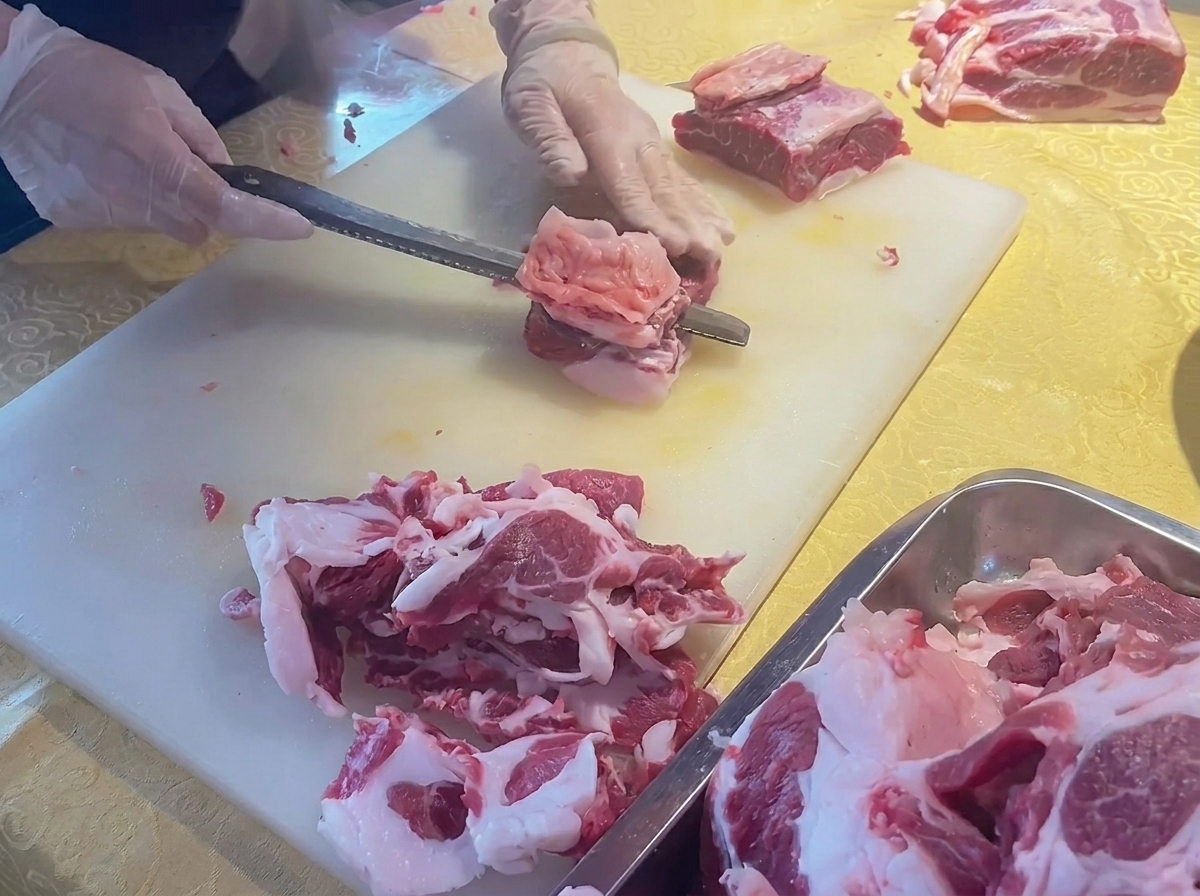 Mani che usano un coltello per rimuovere il grasso in eccesso da un pezzo di costata di manzo fresca su un tagliere bianco.