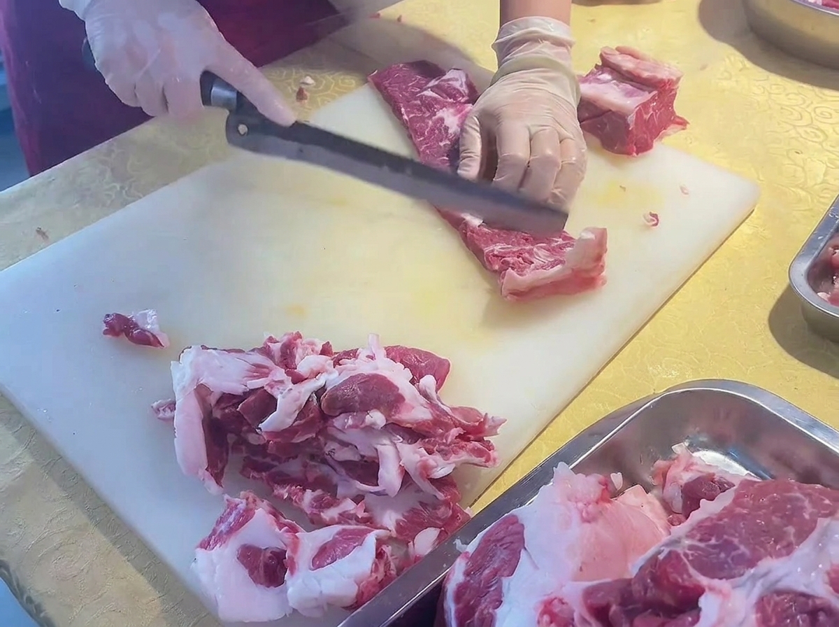 Mani che affettano finemente una costata di manzo mondata, usando un lungo coltello inclinato.