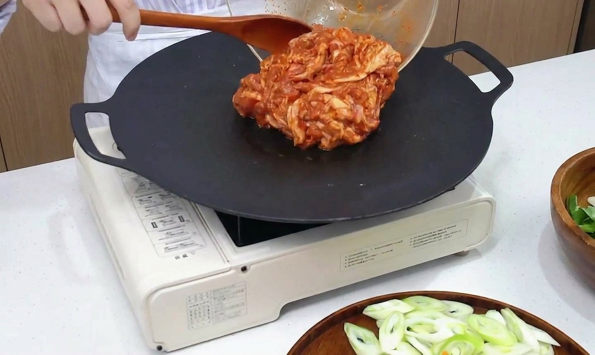 Pancetta di maiale piccante marinata versata da una ciotola di vetro su una piastra nera calda.