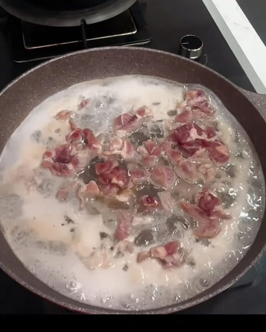 Pezzi di maiale che bollono in una padella con acqua, vino da cucina e una foglia di alloro.