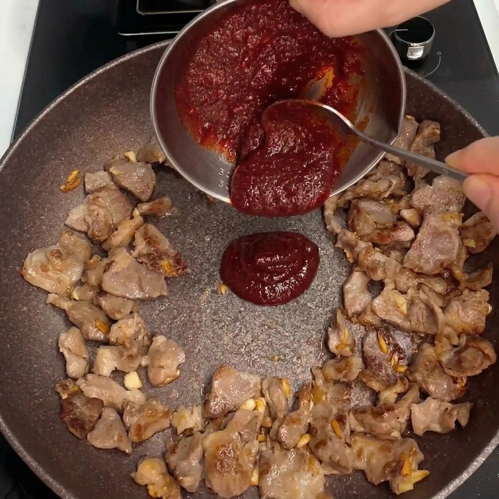 Salsa rossa densa versata al centro della padella con il maiale in cottura.