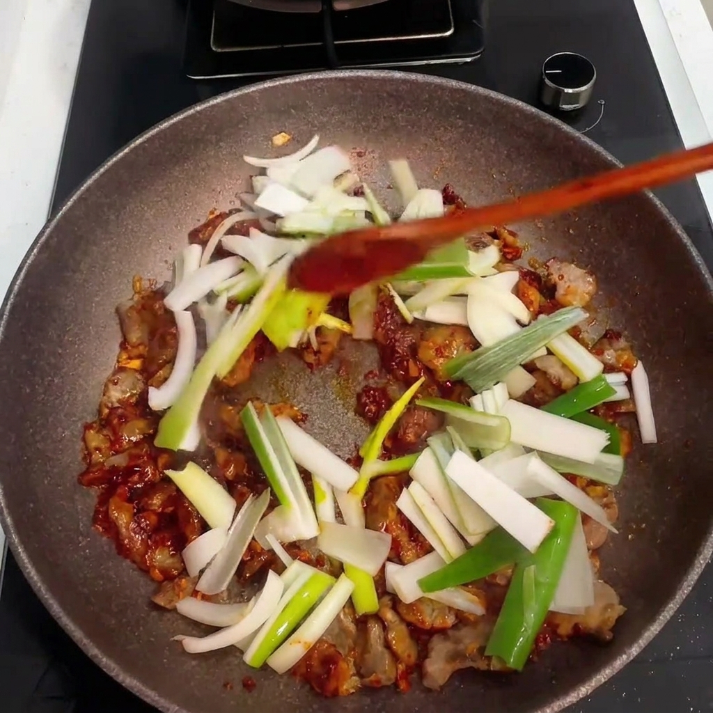 Cipolle e cipollotti tritati aggiunti alla padella con maiale e salsa.
