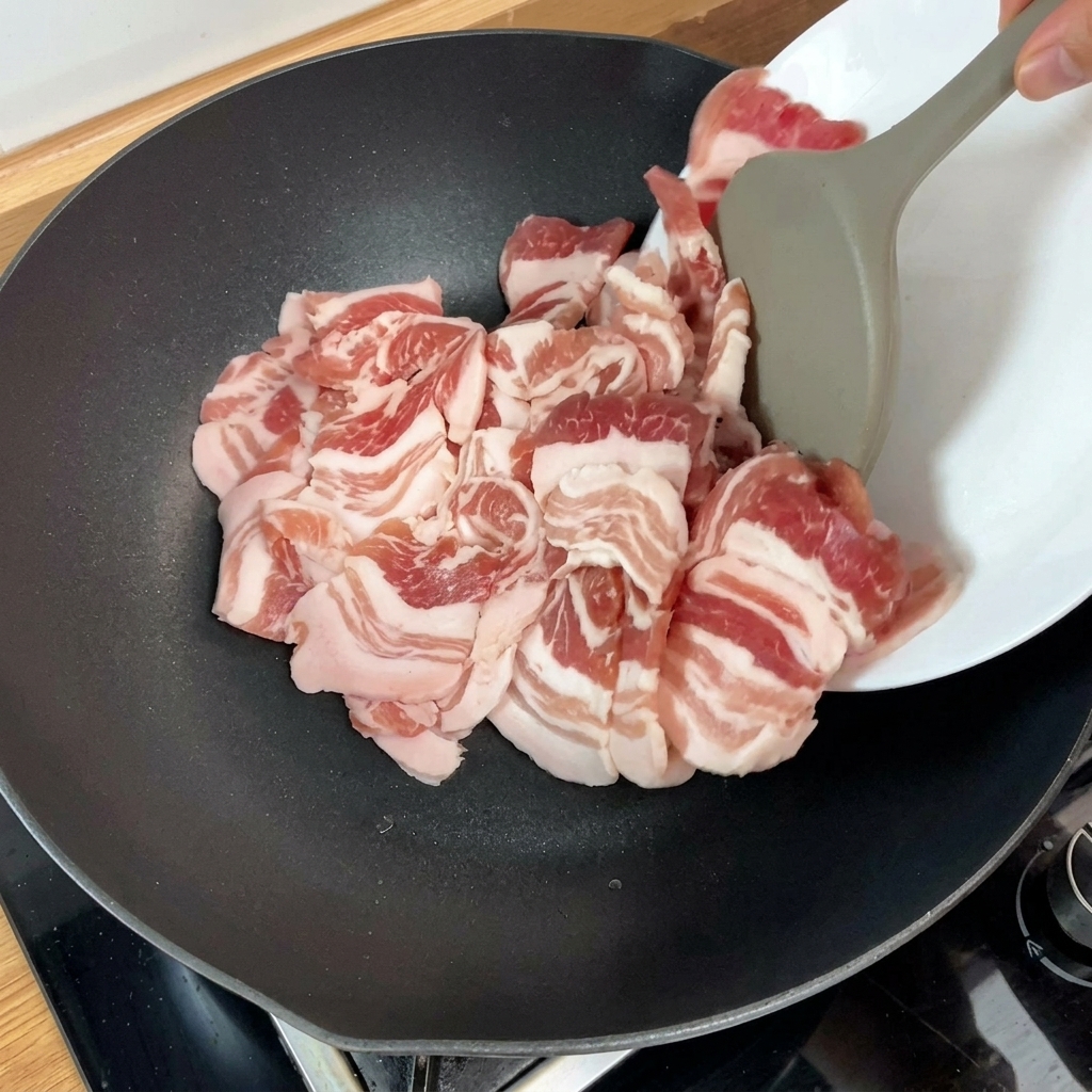 Fette di pancetta di maiale cruda aggiunte in una padella calda con un utensile da cucina.