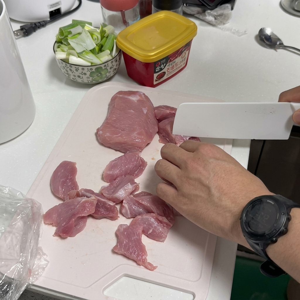 Una persona che affetta maiale crudo su un tagliere di plastica bianco con un coltello da cucina bianco.