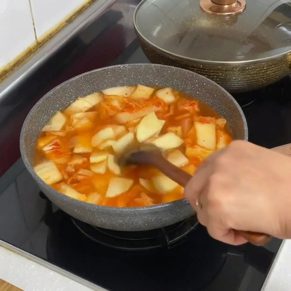 Spaghetti di vetro aggiunti alla pentola di stufato di kimchi gorgogliante.
