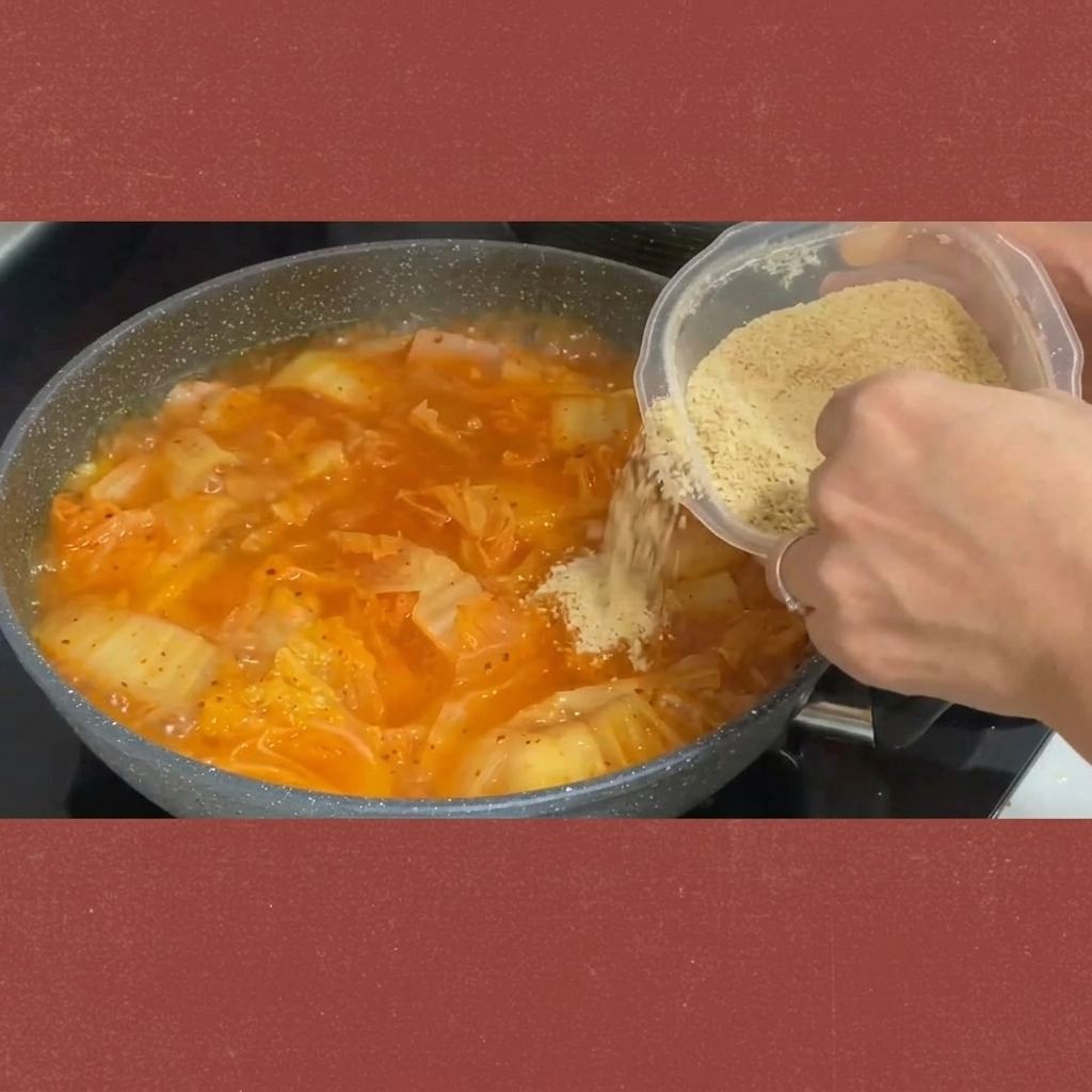 Zucchero cosparso da un contenitore nello stufato di kimchi che sobbolle.