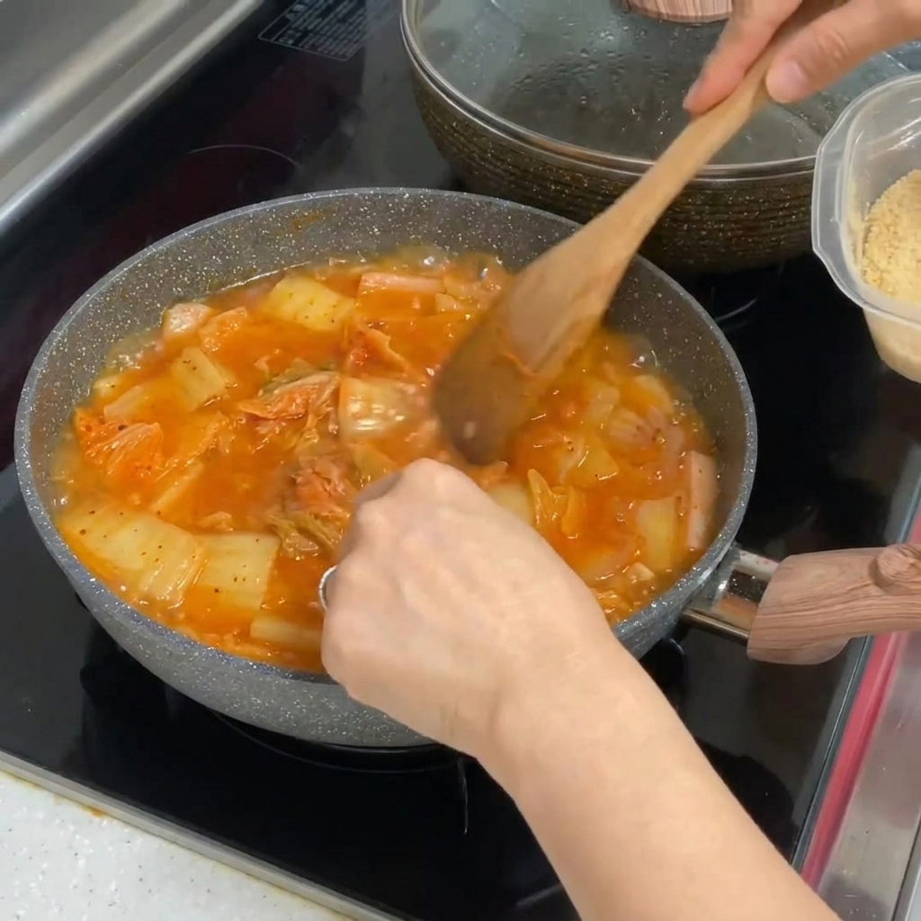 Aglio tritato mescolato in una pentola di stufato di kimchi rosso vibrante.