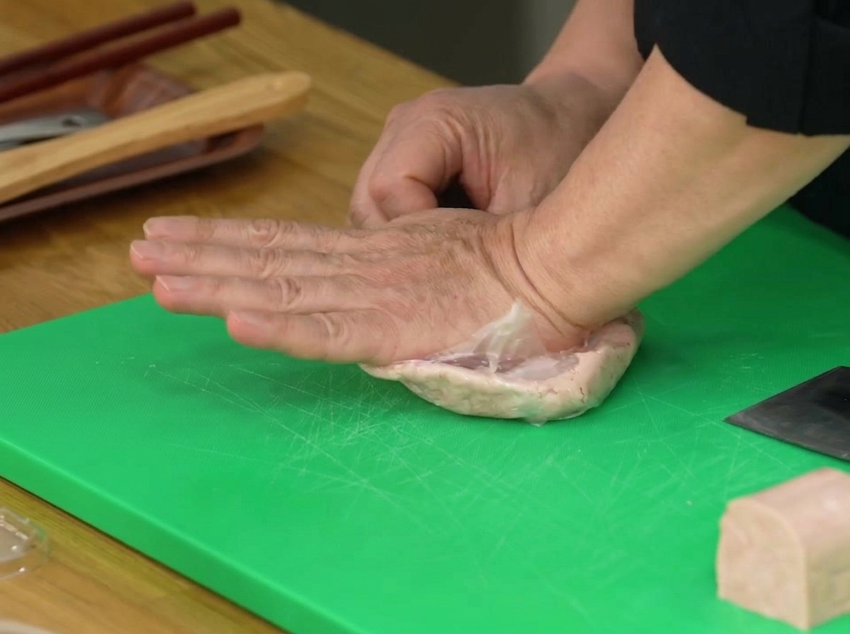 Una mano che preme su un sacchetto di plastica contenente metà blocco di Spam per ridurlo in pasta.