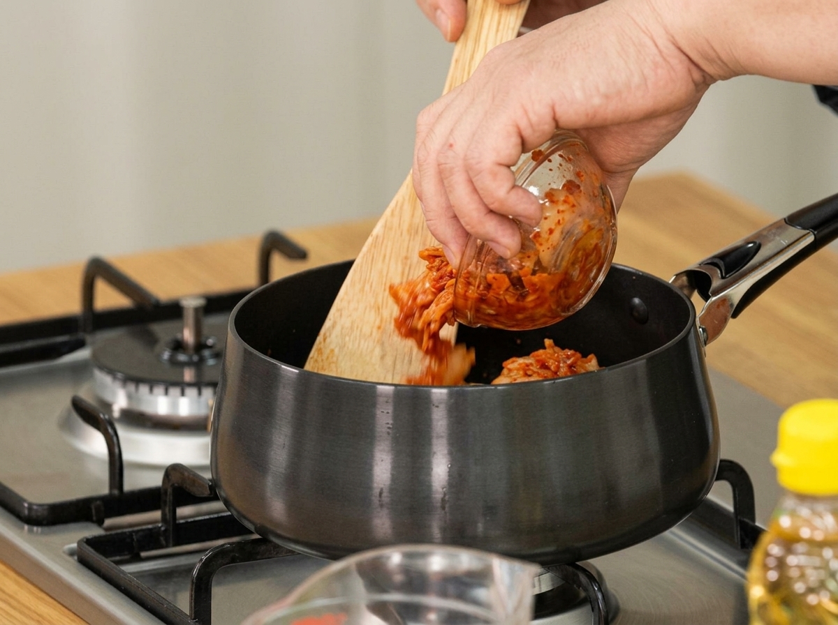 Kimchi invecchiato aggiunto a una pentola con un cucchiaio di legno per saltarlo.