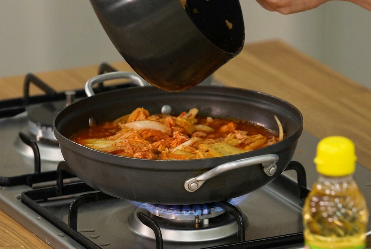 Fette di tofu morbido e scalogno fresco disposti delicatamente sulla superficie dello stufato di kimchi che sobbolle.