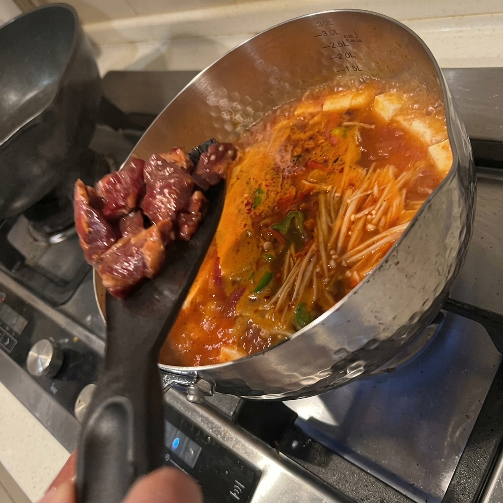 Pezzi di manzo marinato immersi nella pentola di zuppa di kimchi e tofu in ebollizione.