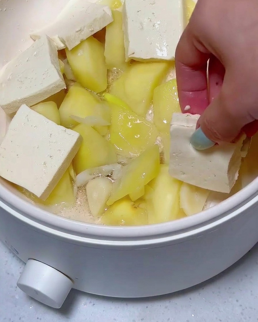 Fette di tofu e carne in scatola disposte sopra pezzi di patata nella pentola.