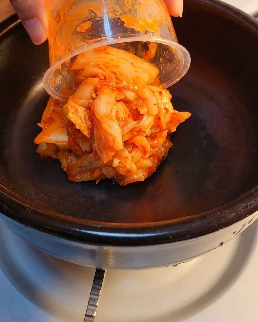 Kimchi fermentato e carne in scatola schiacciata stratificati in una pentola di pietra.