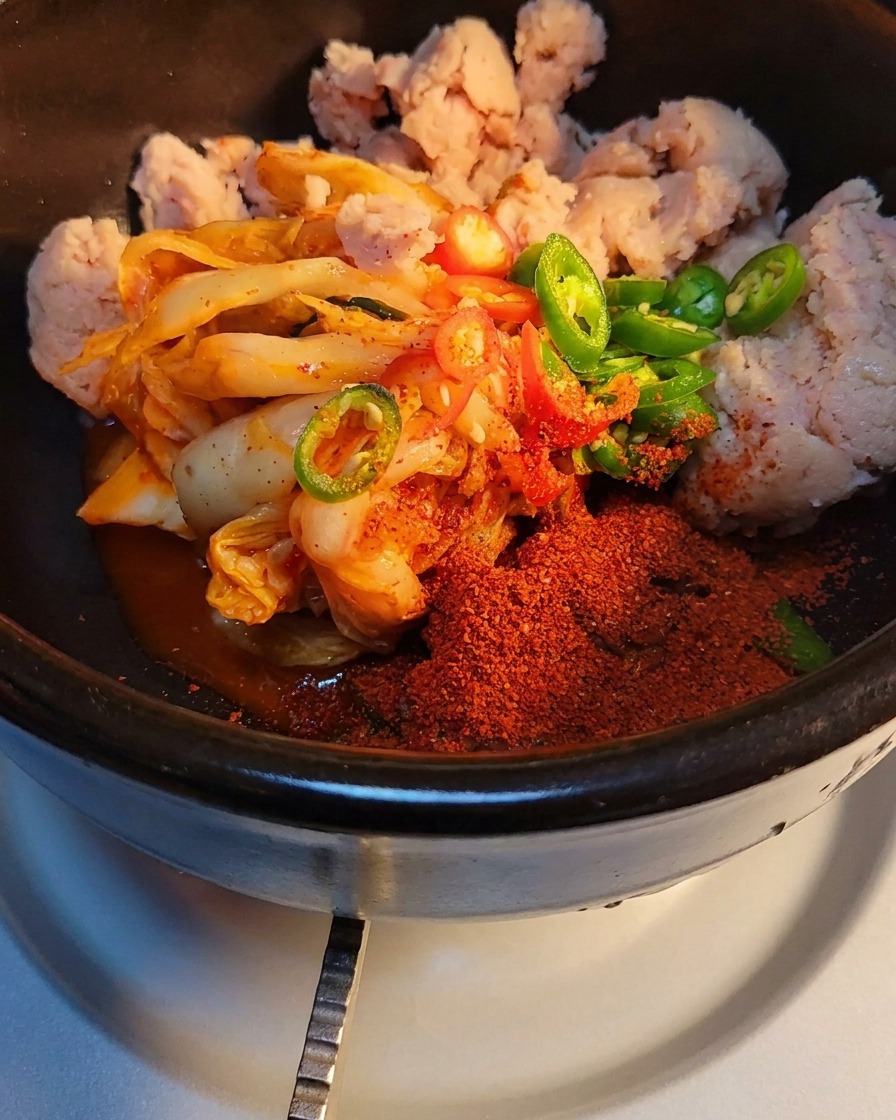 Dettaglio di zucchero e preparato per brodo di manzo cosparsi su kimchi e carne in scatola in una pentola di pietra.