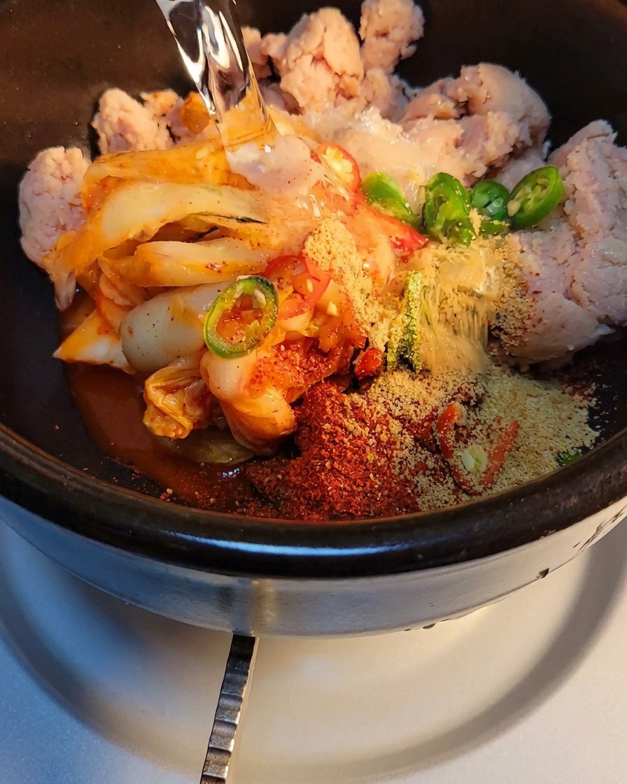 Acqua versata nella pentola di pietra con kimchi e spezie, pronta per essere riscaldata sul fornello.