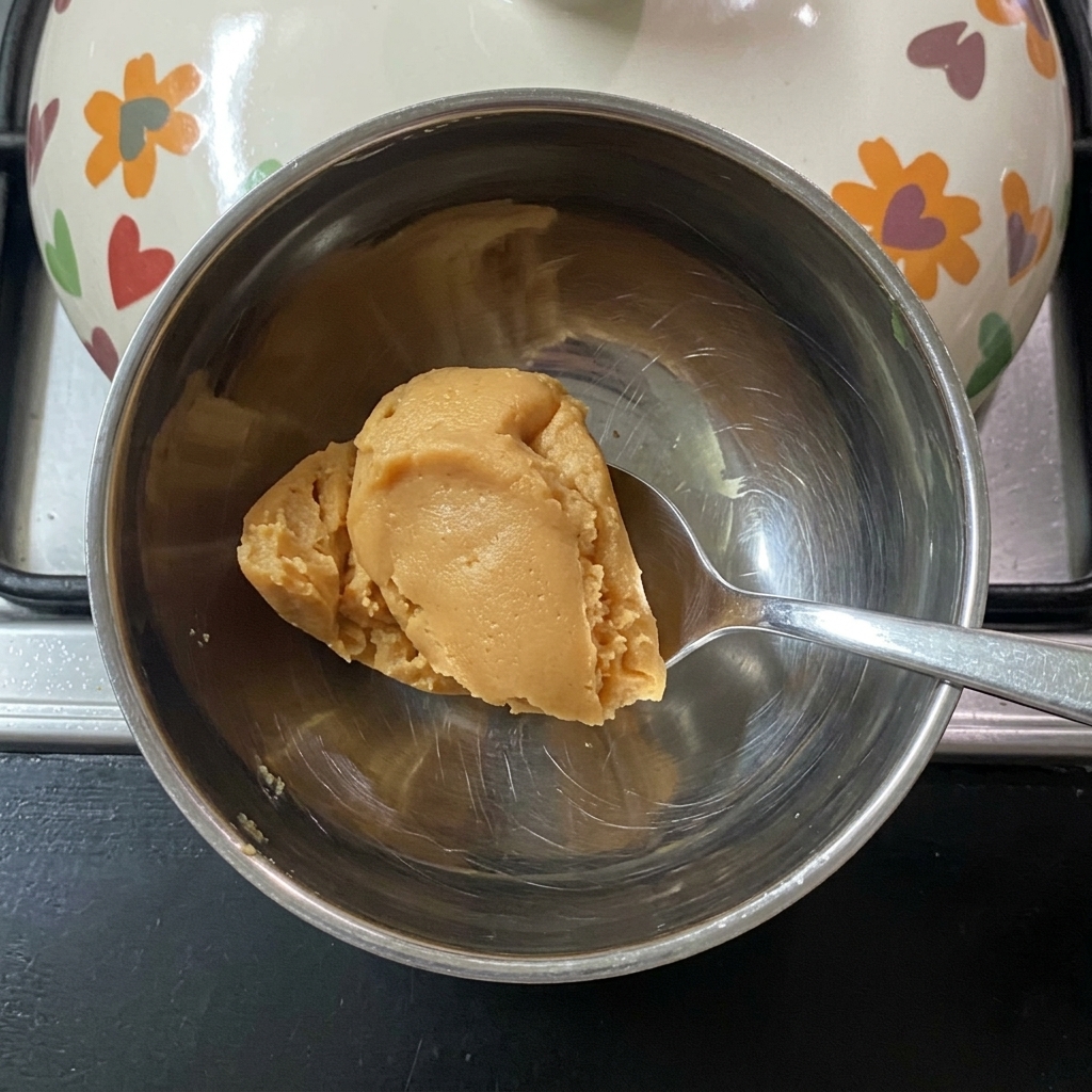 Un cucchiaio che mescola pasta di miso in acqua tiepida allinterno di una piccola ciotola di metallo.
