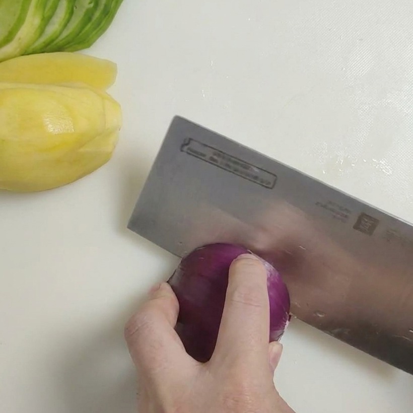 Un coltello affilato che taglia una cipolla rossa a cubetti grossolani su un tagliere.