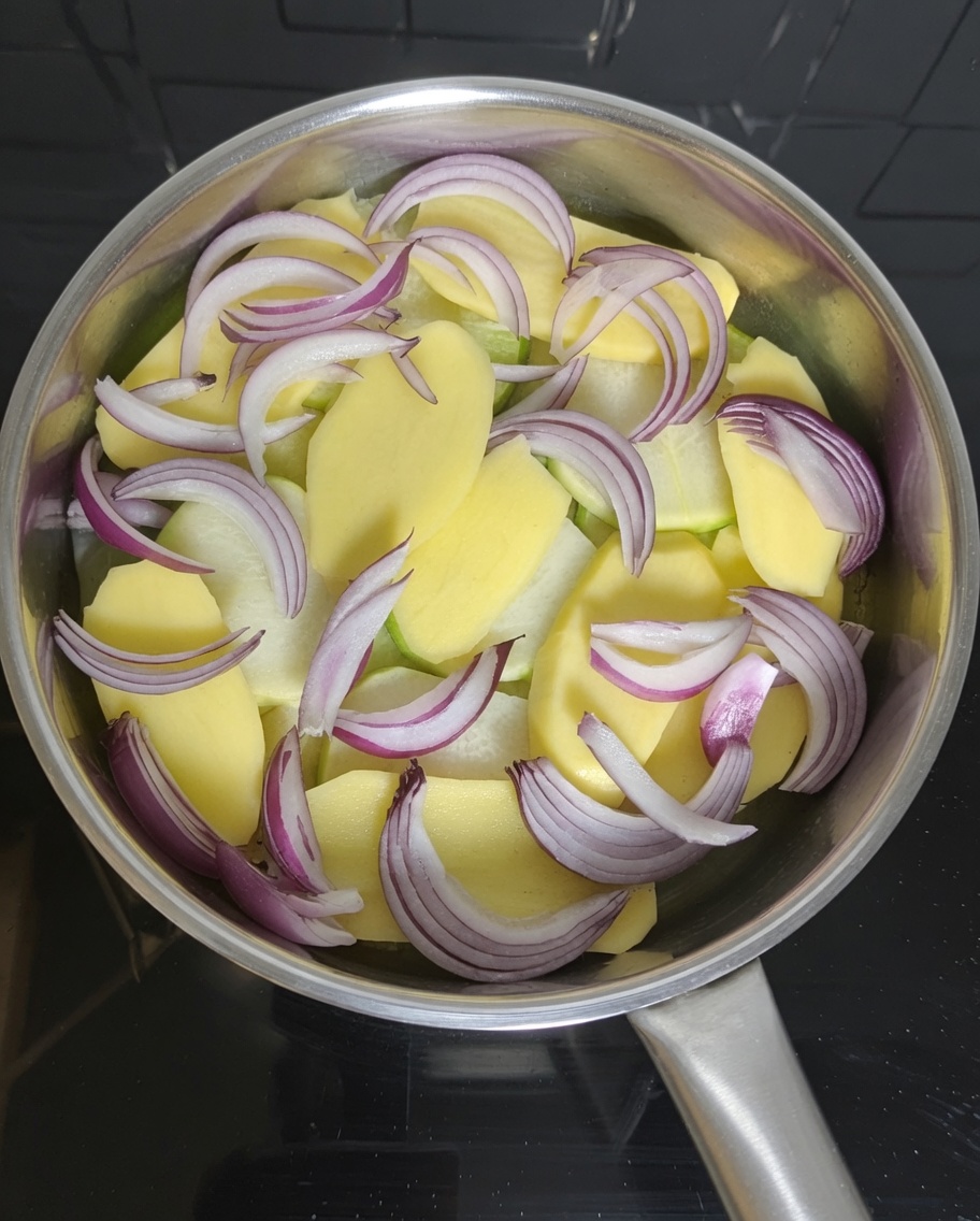 Pezzi di sgombro in scatola disposti sopra le fette di patate e cipolla in una pentola.