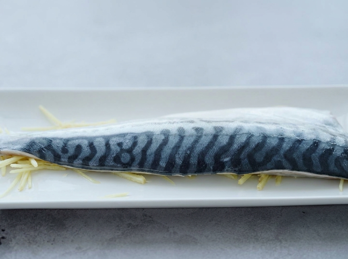 Un filetto di sgombro sopra strisce di zenzero con sake versato sopra.