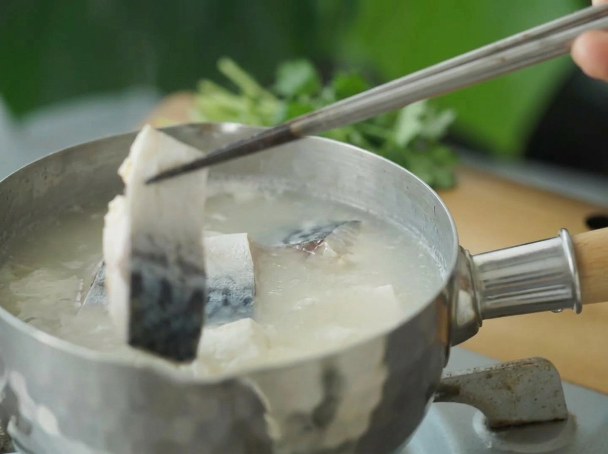Pezzi di sgombro sbollentati immersi nella zuppa bollente con le bacchette.
