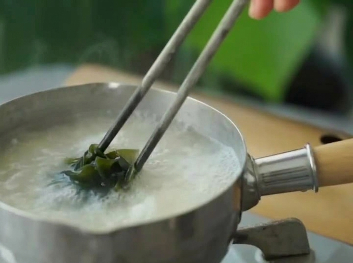 Wakame verde reidratato aggiunto alla zuppa di miso in cottura con le bacchette.
