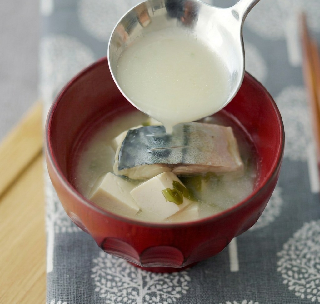 Zuppa di miso con sgombro e tofu servita in una ciotola di ceramica rossa profonda.