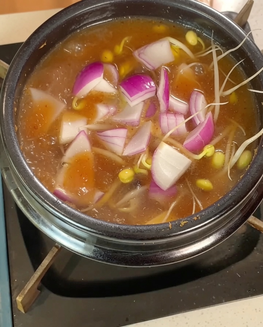 Germogli di soia, cipolla a fette e cubetti di tofu immersi nel brodo bollente.