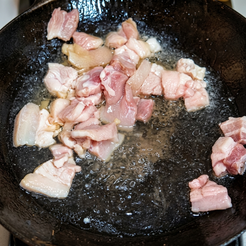 Pezzi di pancetta di maiale dorati che friggono nello strutto fuso in un wok tradizionale.