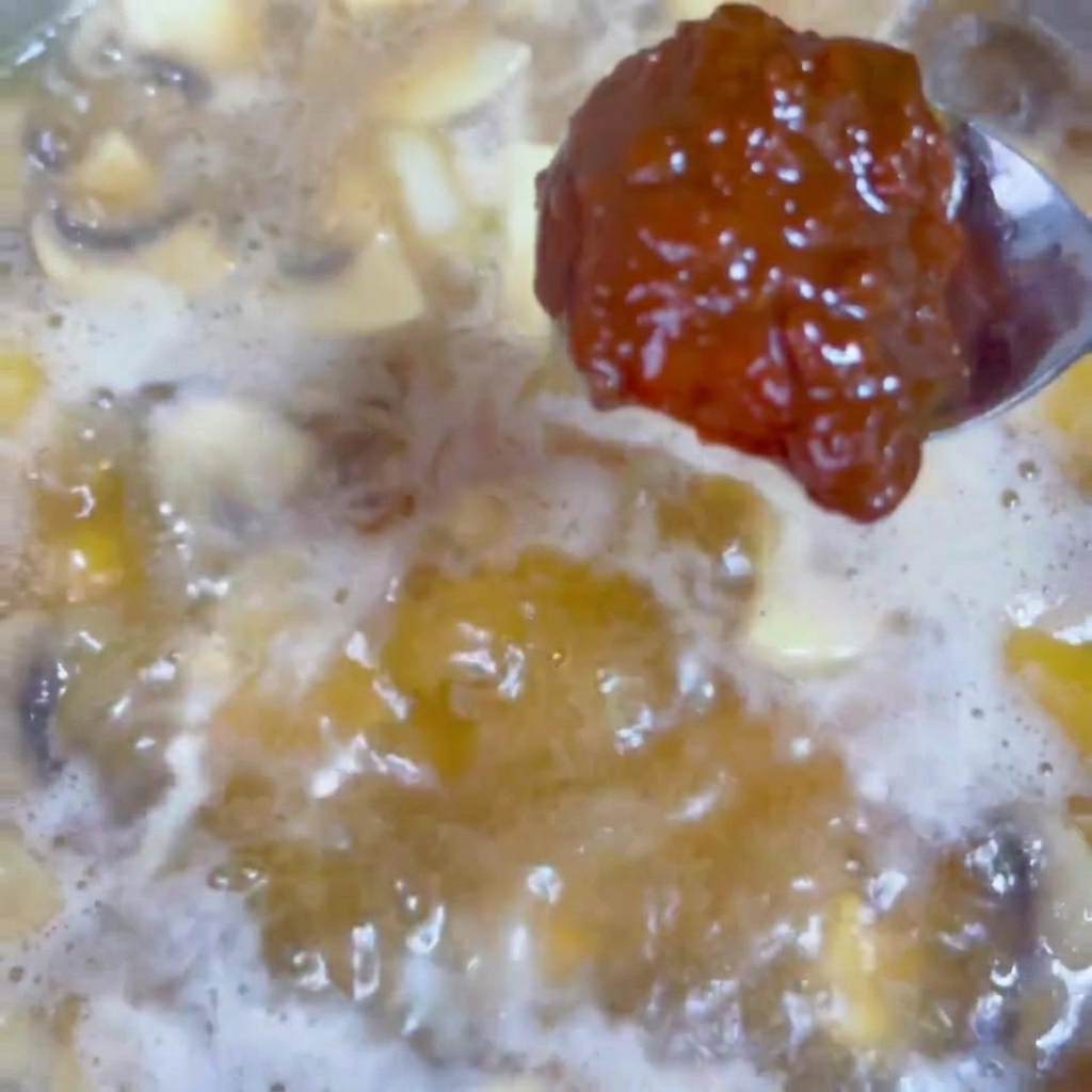 Un cucchiaio di pasta di soia scura che viene incorporato in un brodo bollente nel wok.