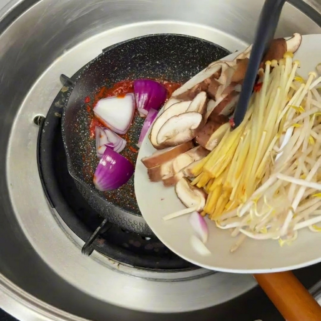 Olio di sesamo versato da un cucchiaio in una pentola di stufato di manzo e tofu bollente e aromatico.