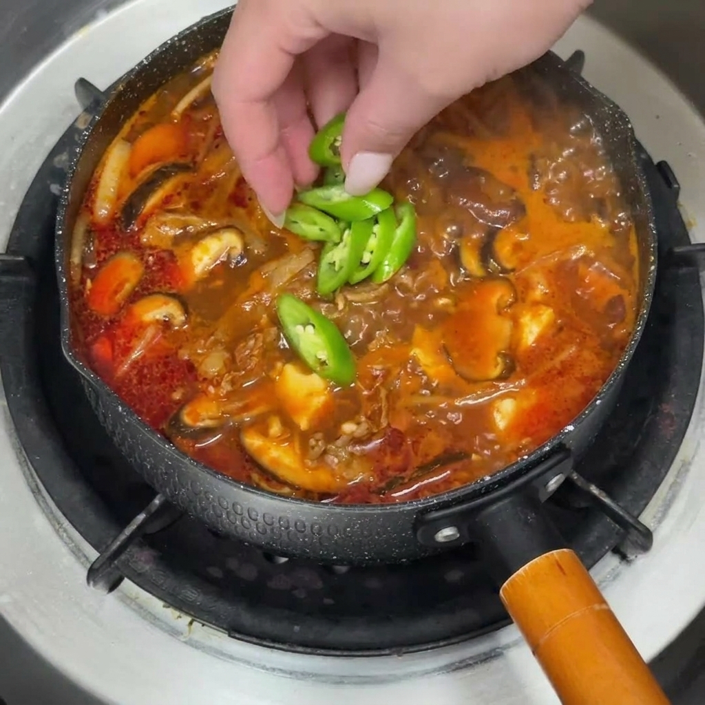 Una pentola di stufato di manzo guarnita con fette di peperoncino verde vibrante e cipollotti freschi tritati.