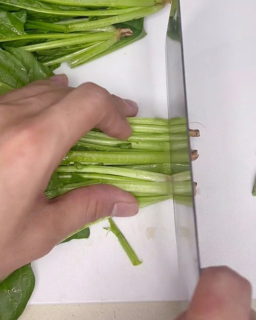 Un mazzo di spinaci verdi freschi su un tagliere bianco pulito, pronti per essere mondati con un coltello.