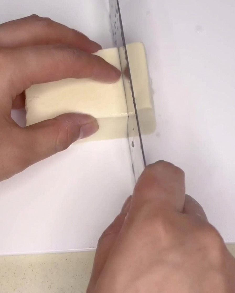 Un panetto di tofu bianco sodo che viene tagliato a piccoli rettangoli con un grande coltello da cucina su un tagliere.