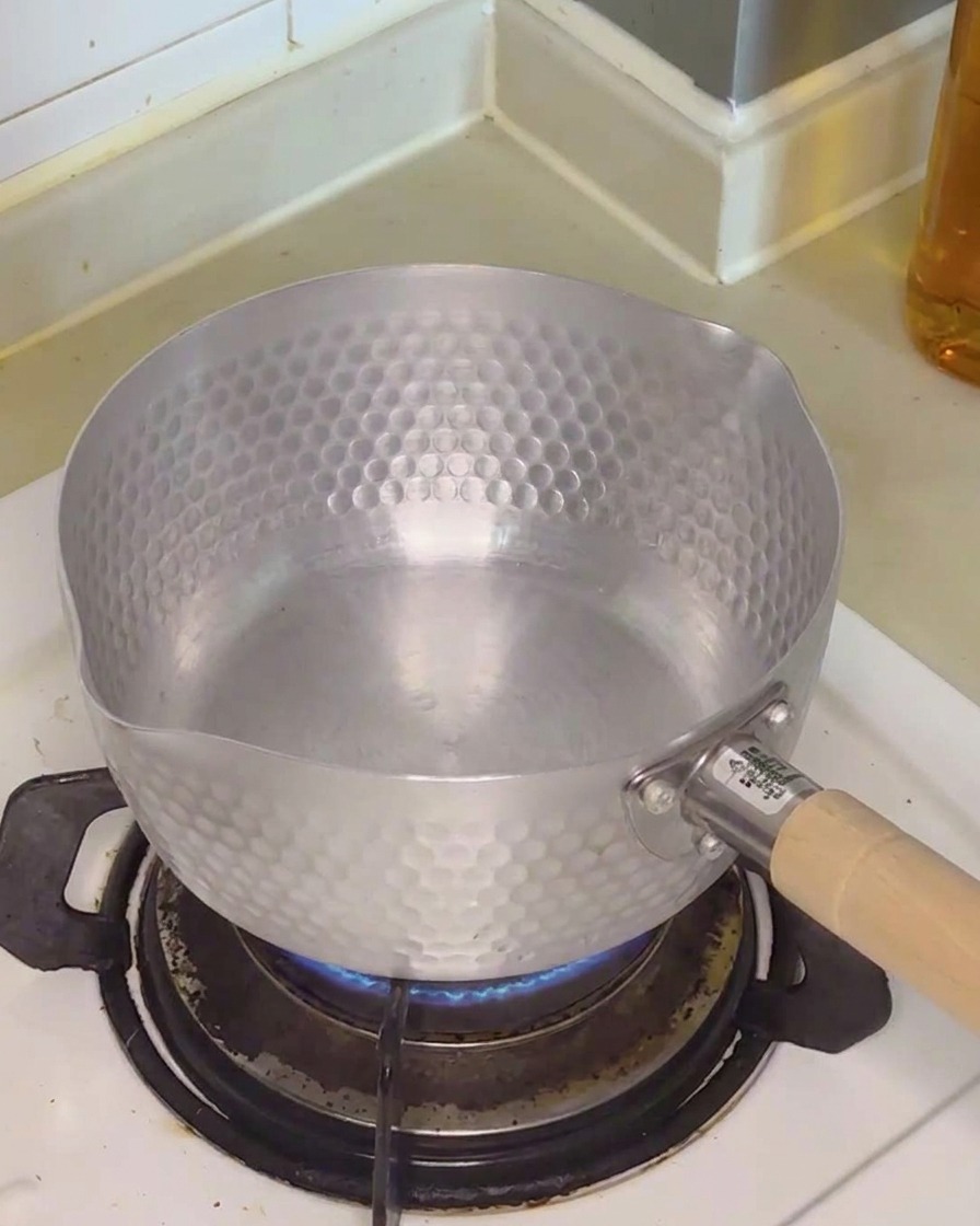 Acqua limpida versata in una piccola pentola di metallo martellato posta sul fornello a gas.