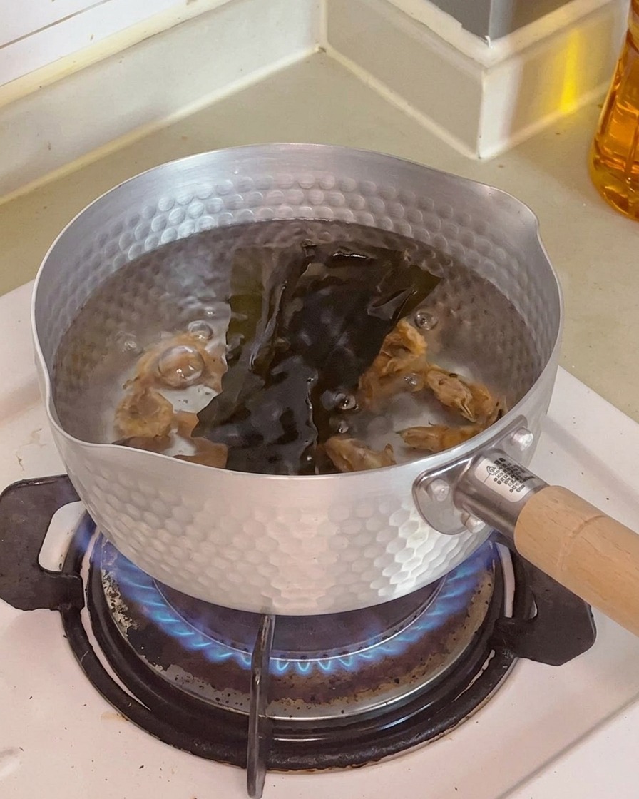Primo piano di gamberi essiccati e un pezzo di alga kelp scura immersi nellacqua dentro una pentola.