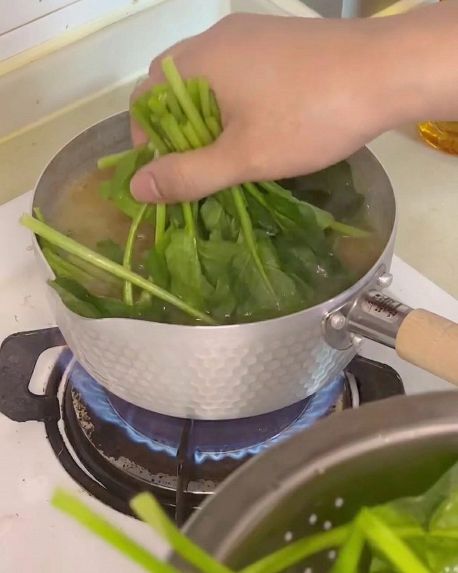 Spinaci freschi, cubetti di tofu e funghi enoki aggiunti nella pentola di zuppa in ebollizione.