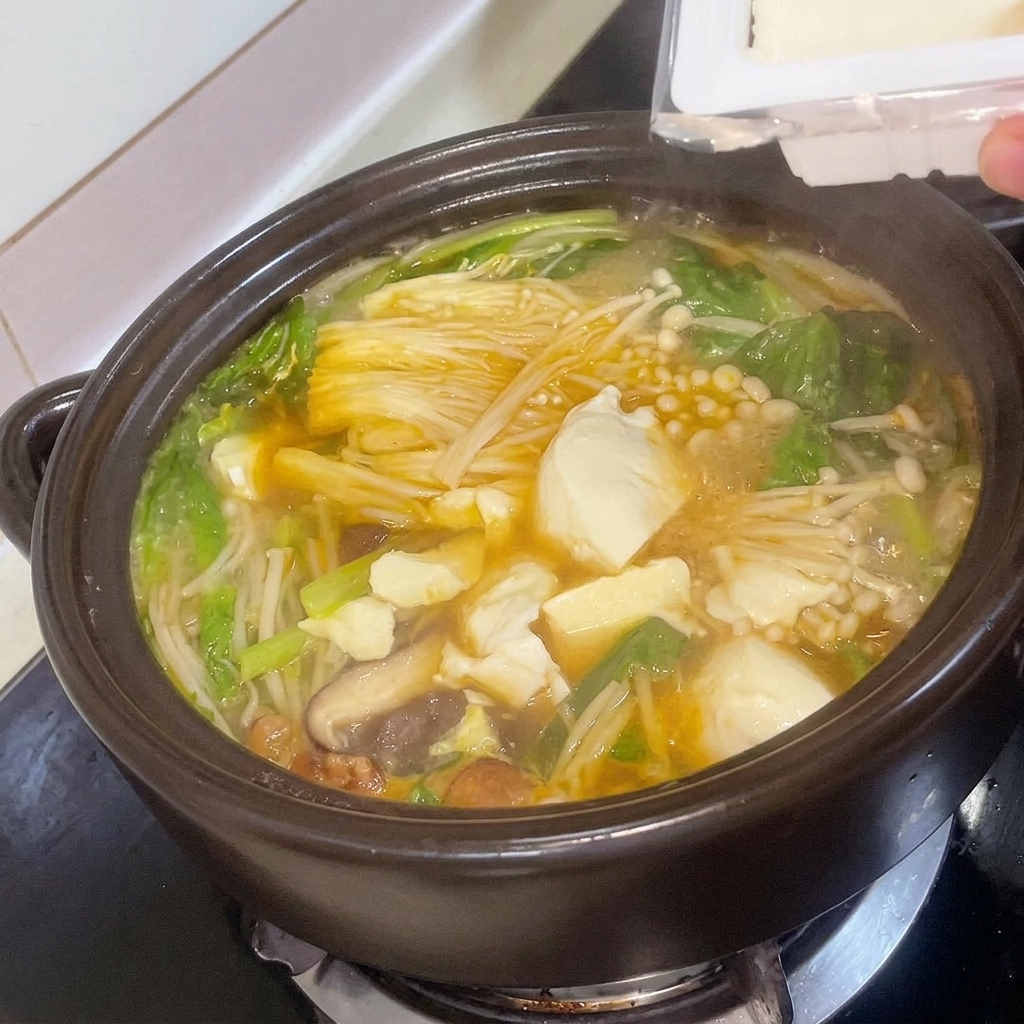 Cubetti di tofu fresco aggiunti con cura allo stufato di pasta di soia coreano che sobbolle nel tegame.