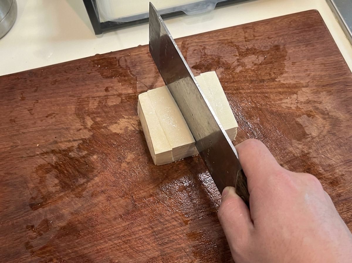 Un blocco di tofu compatto tagliato in cubetti uniformi su un tagliere.