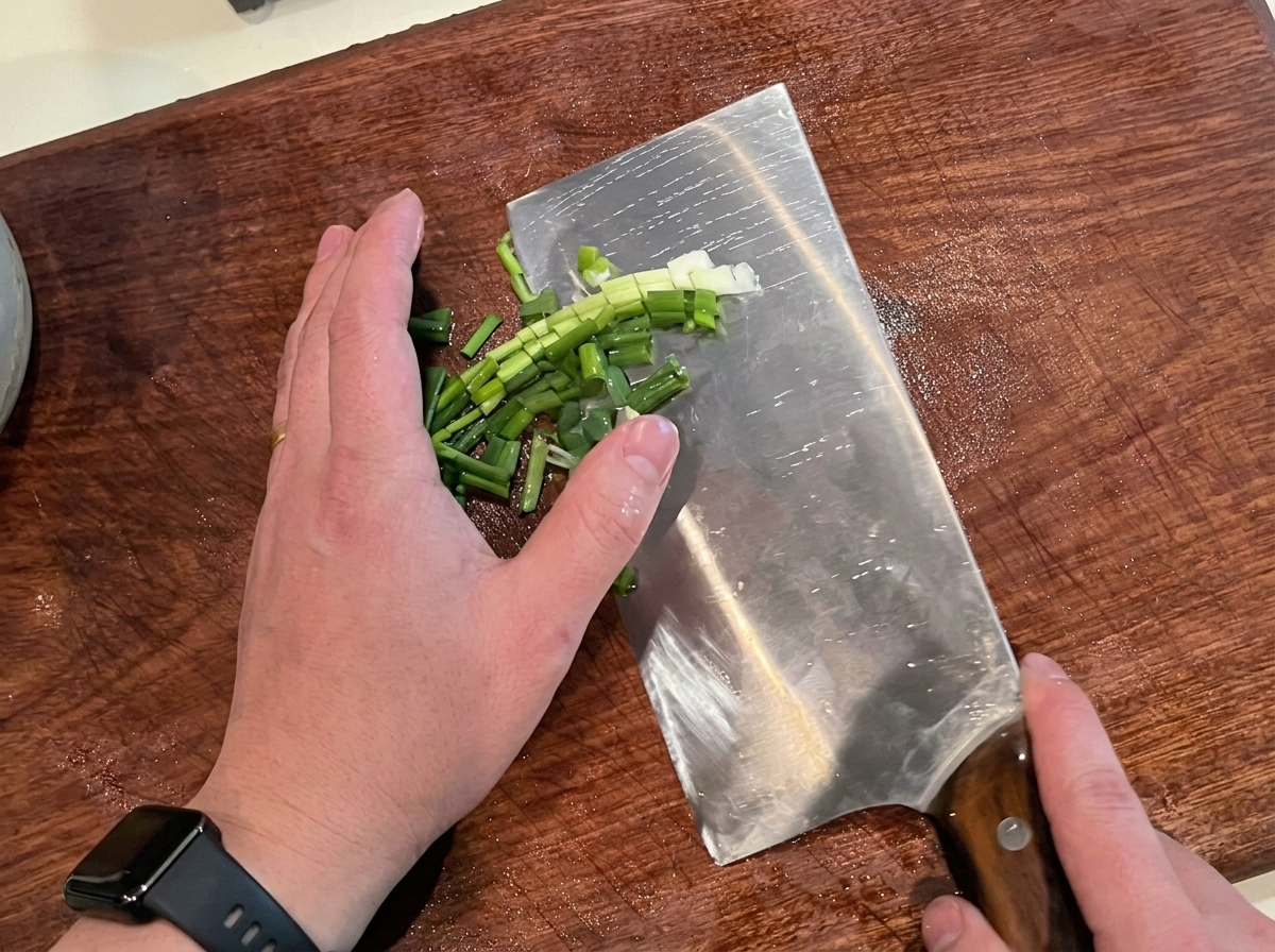 Cipollotti freschi tritati finemente su un tagliere di legno.