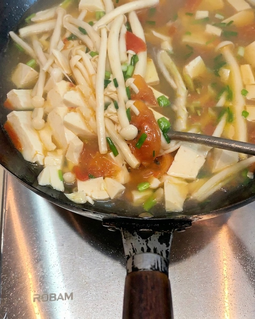 Pomodori che cuociono in un wok con strutto fuso, iniziando ad ammorbidirsi e rilasciare i succhi.