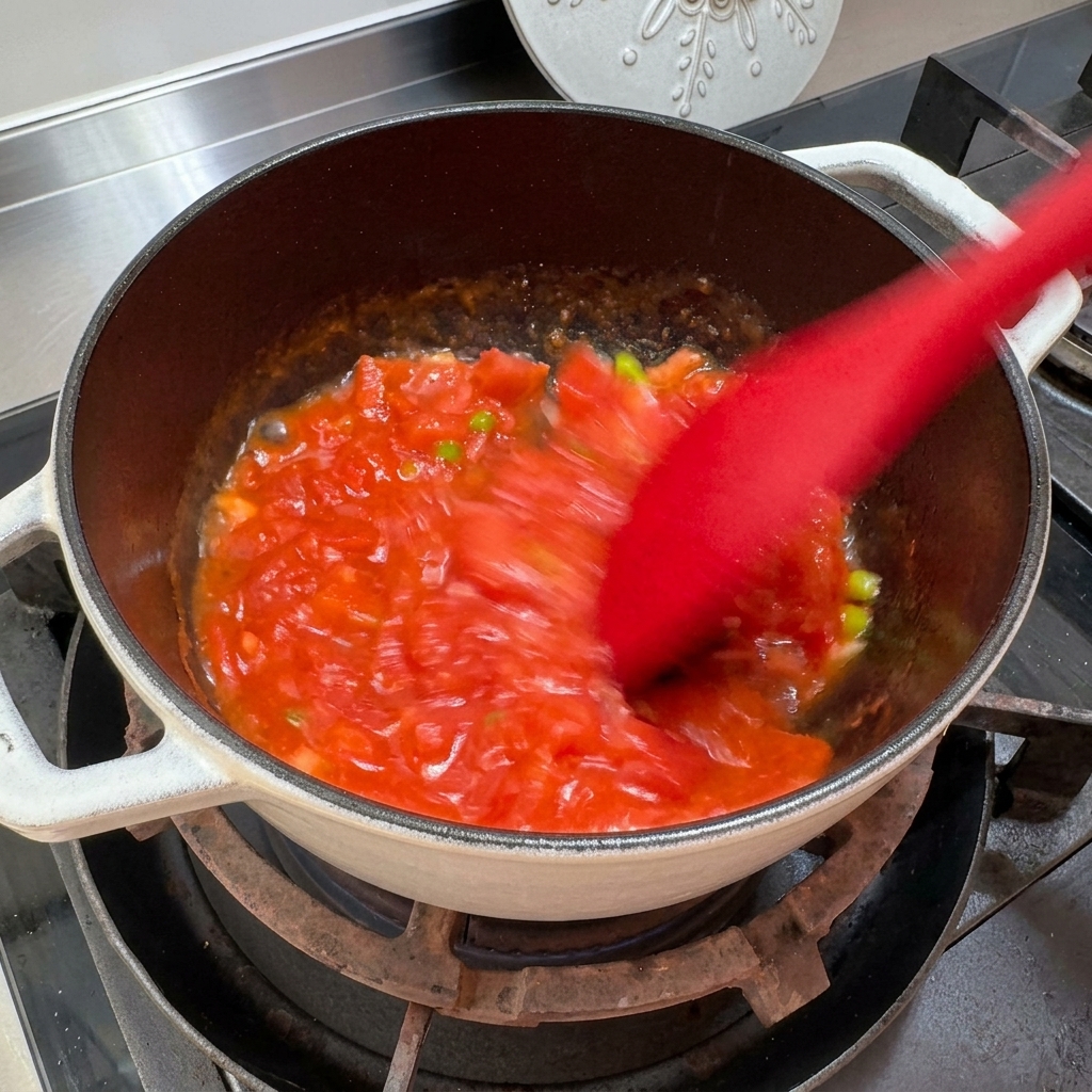 Pomodori schiacciati e mescolati in pentola per creare una consistenza simile a una salsa.