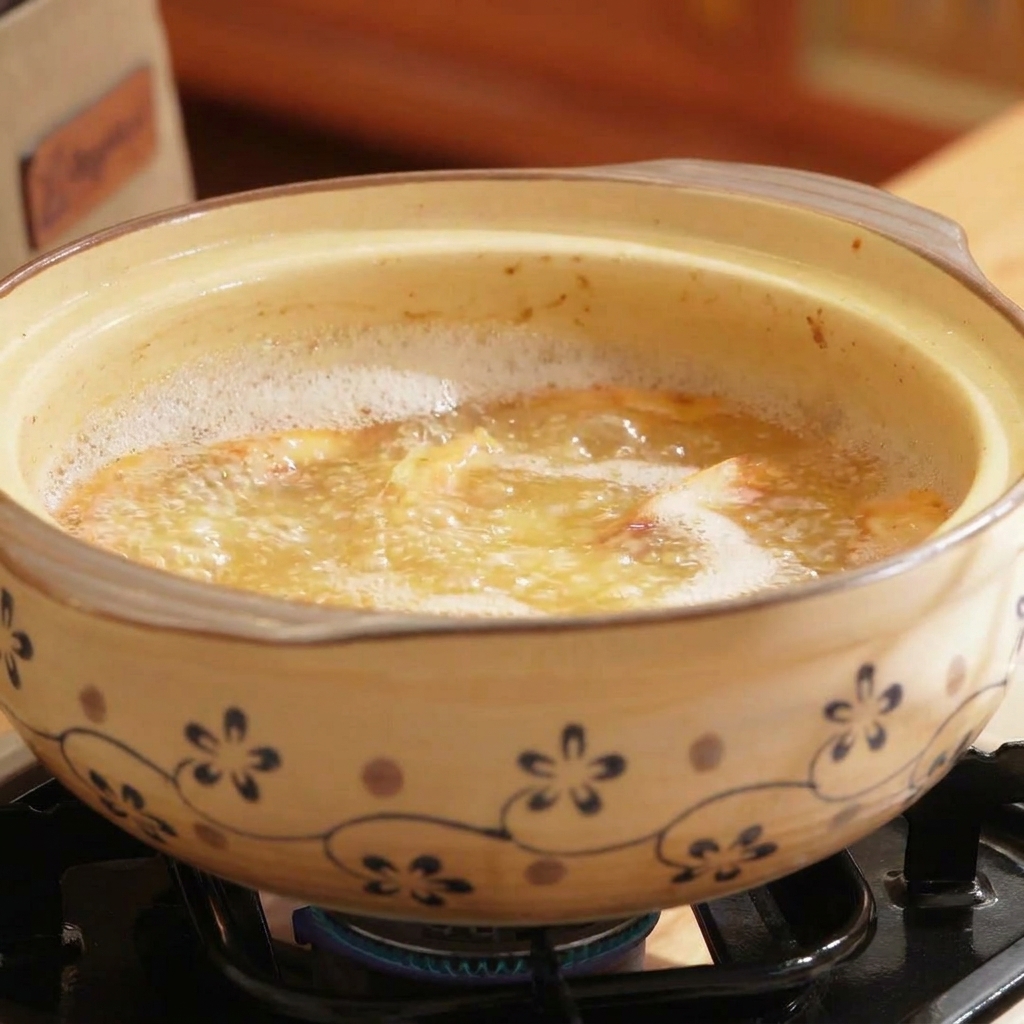 Un vaso di terracotta pieno di brodo bollente color arancione, con funghi frutti di mare e shiitake aggiunti.