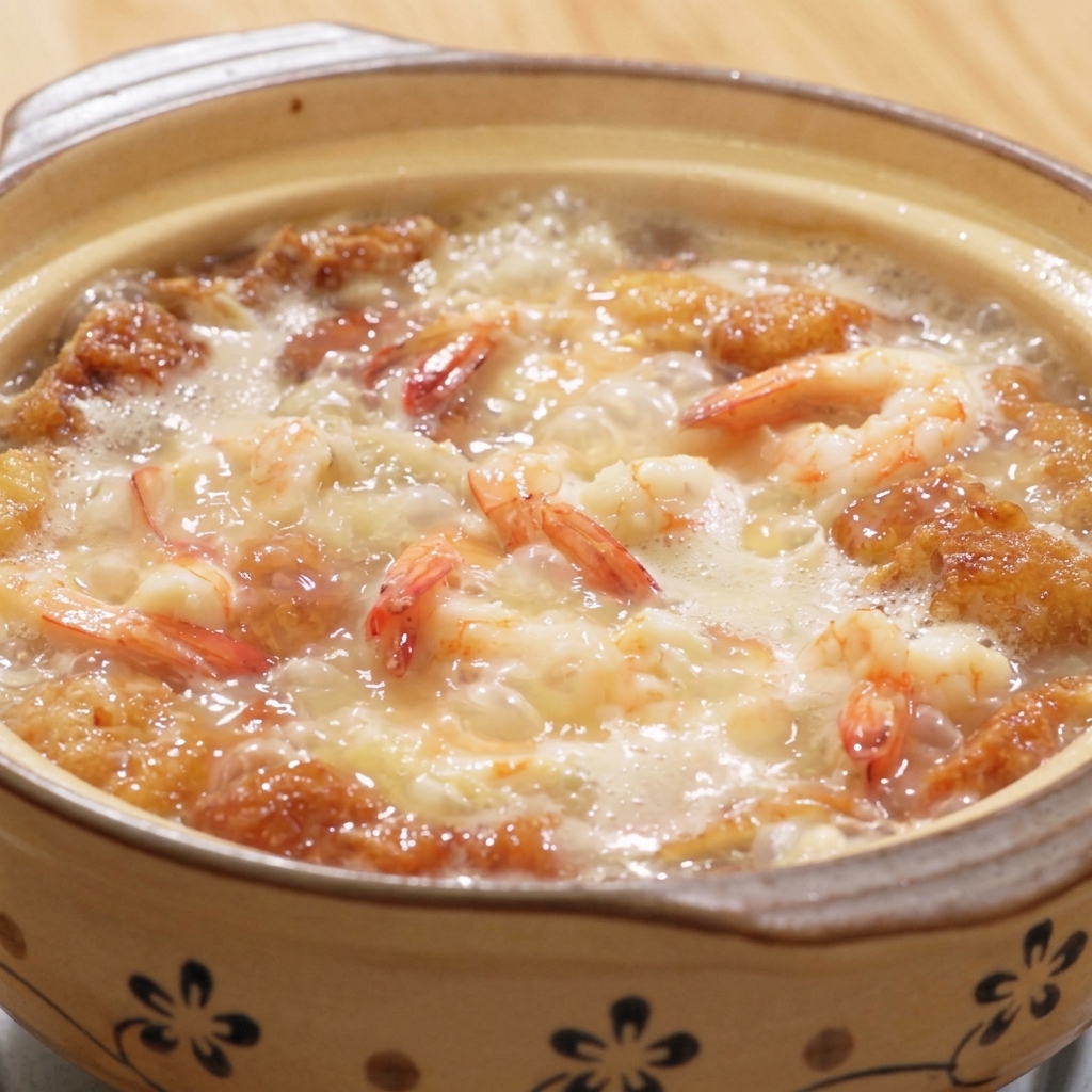 Un vaso di terracotta fumante di zuppa con gamberi, tofu e uova, condita con pepe bianco e sale.