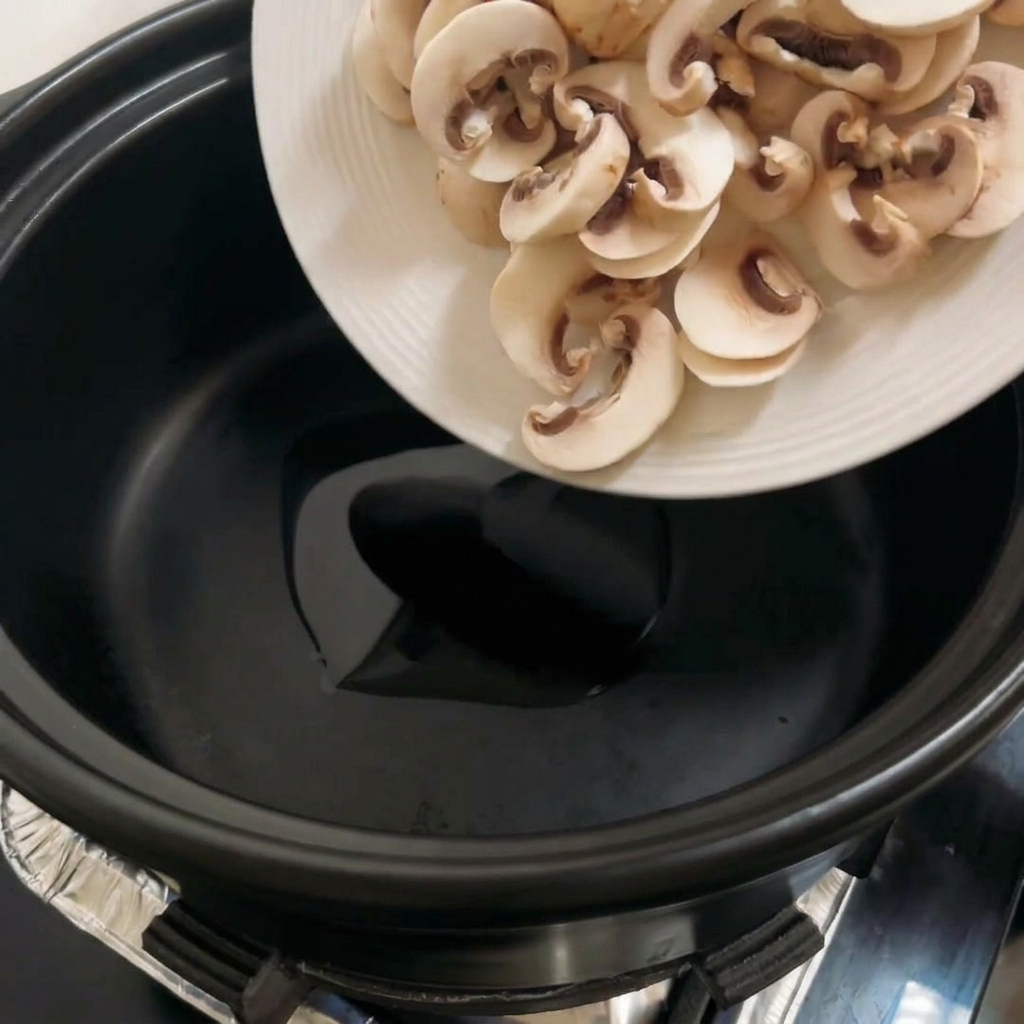 Funghi portobello affettati che cuociono in una pentola nera, diventando dorati.