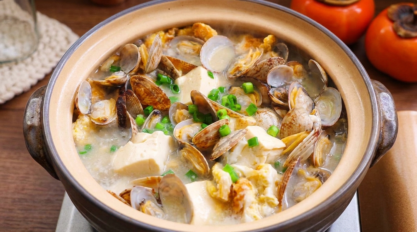 Una pignatta fumante di zuppa di vongole e tofu, guarnita con cipollotti freschi.