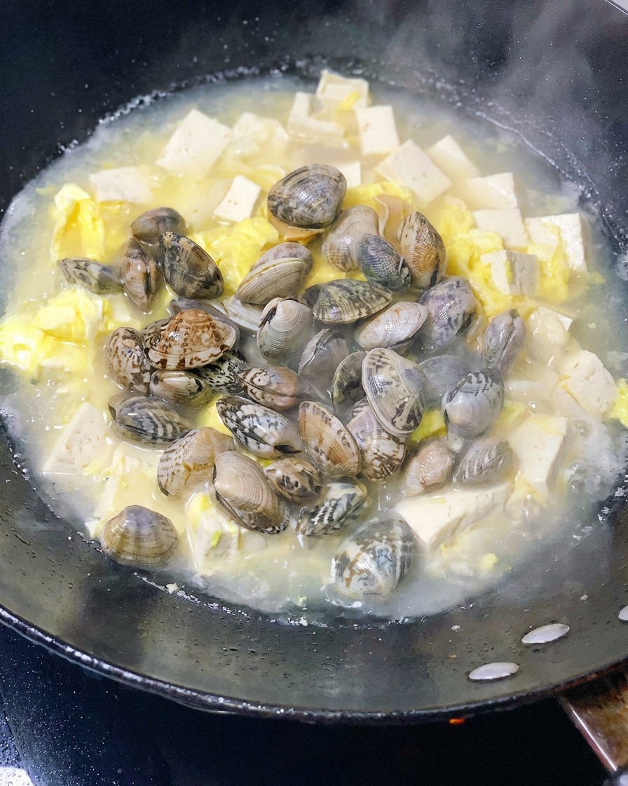 Vongole fresche aggiunte alla pentola con il tofu e le uova.