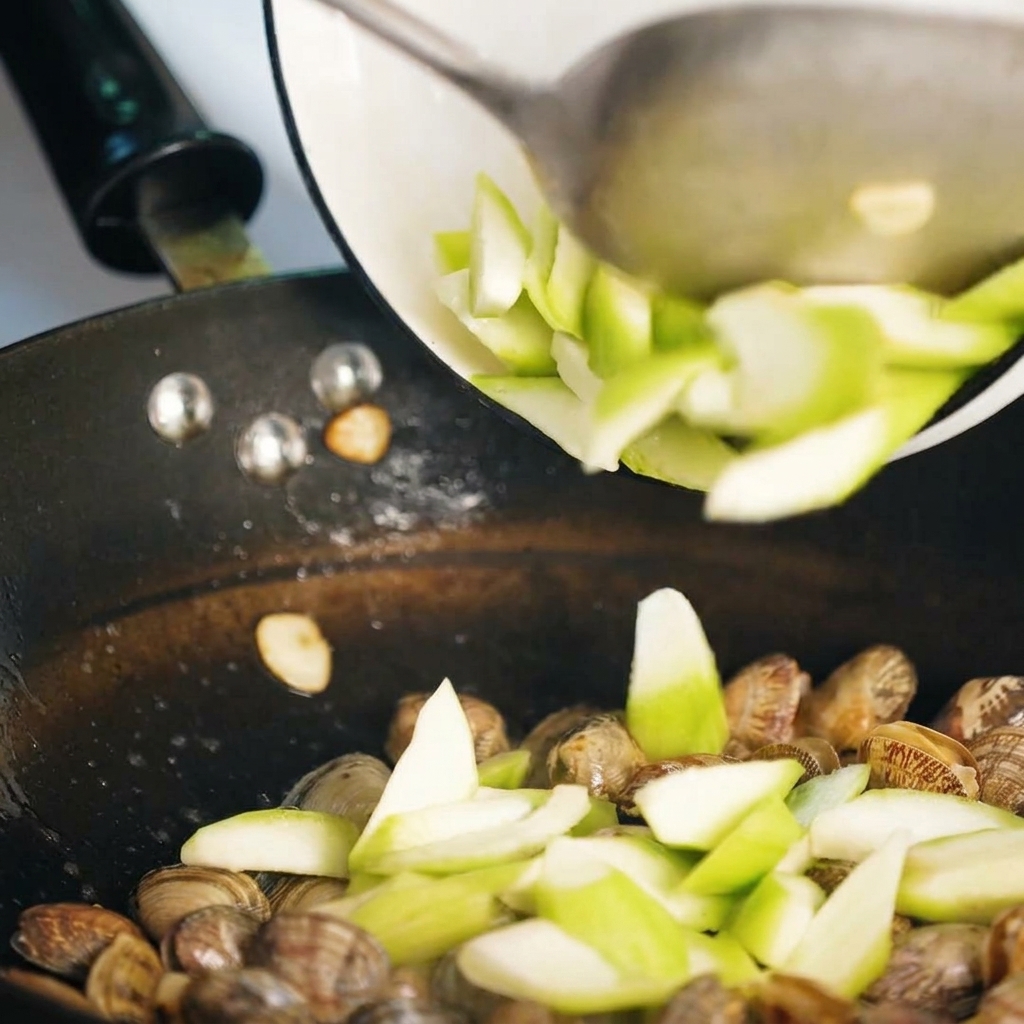 Fette di luffa saltate insieme alle vongole nella padella.