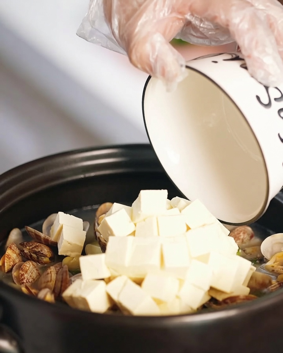 Cubetti di tofu e pezzi di uova fritte aggiunti alla zuppa nella pentola.
