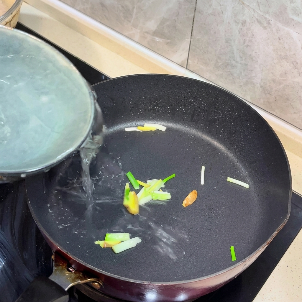 Acqua bollente versata in una padella con zenzero e cipollotti soffritti.